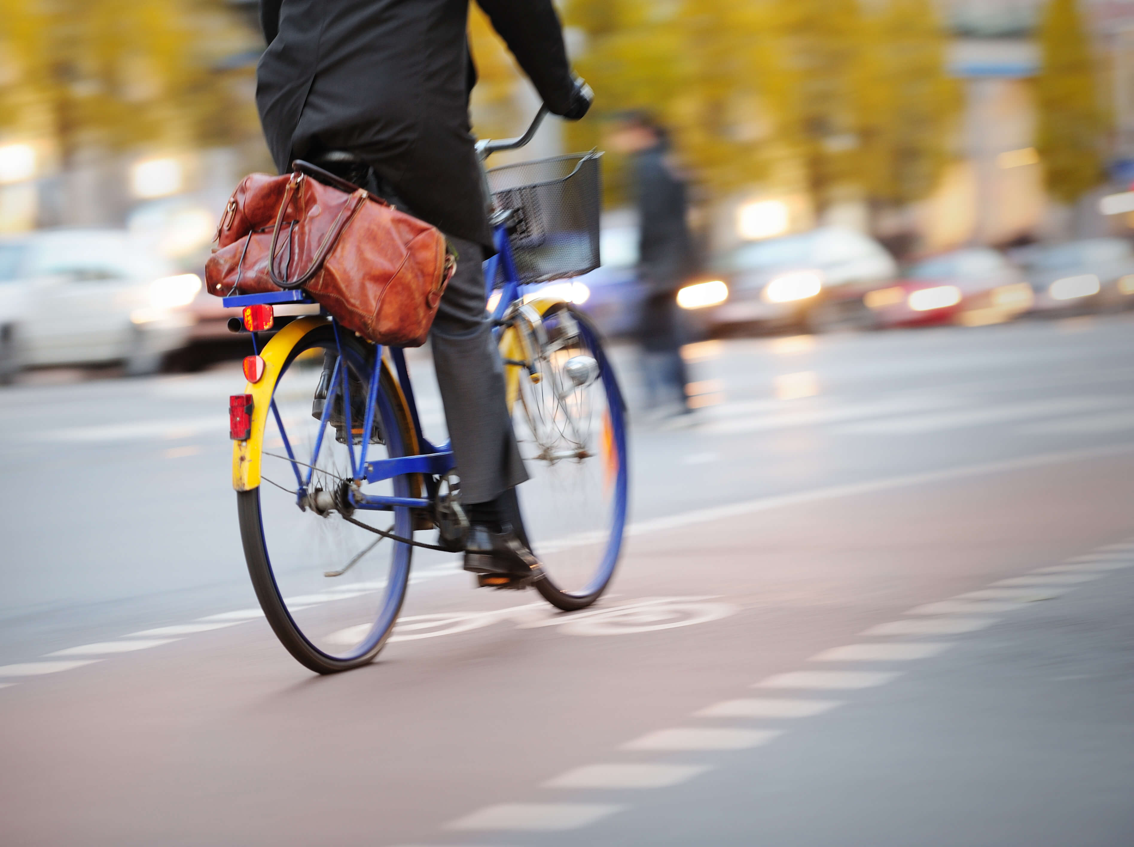 A man rides a blue and yellow bicycle along a busy road