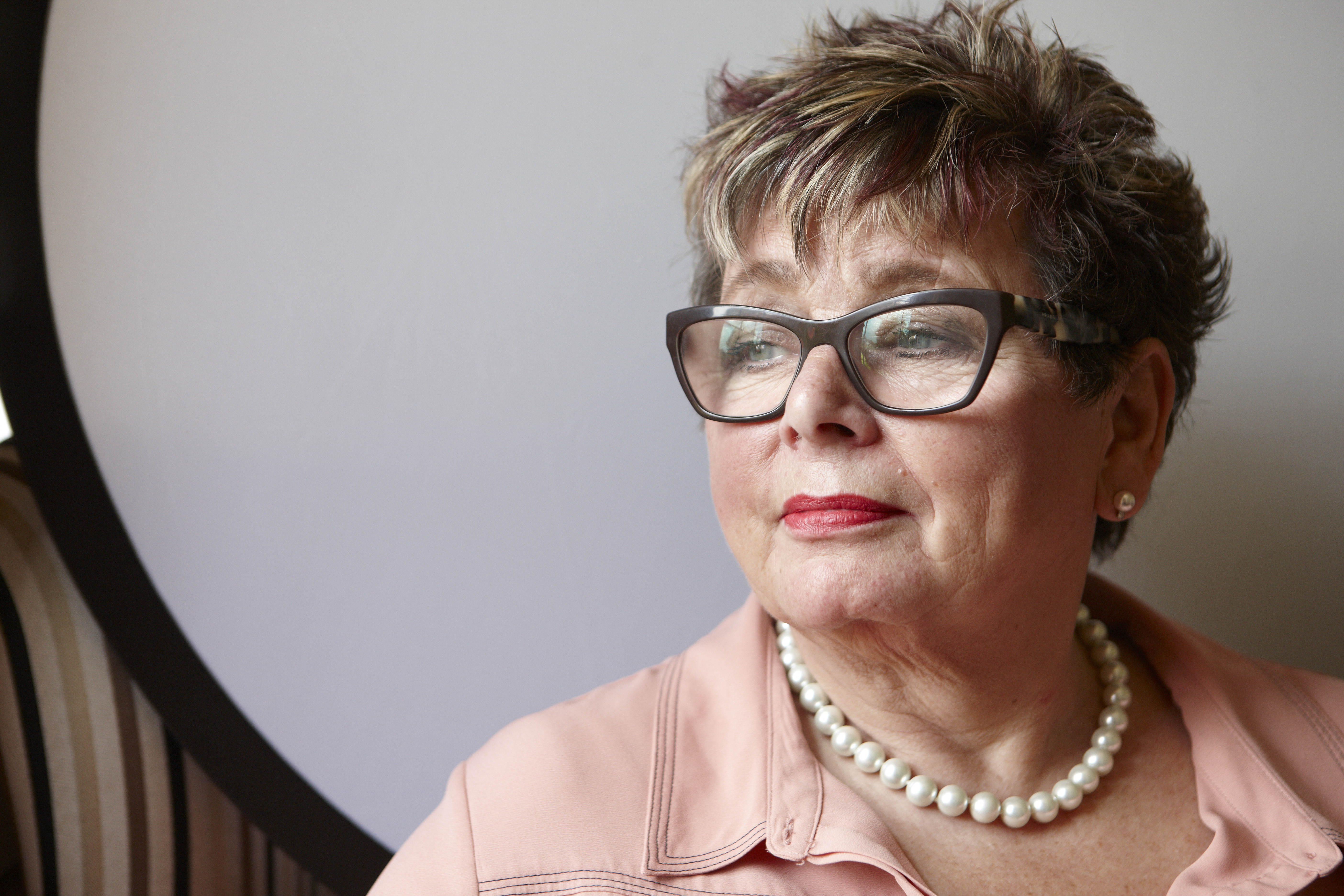 A woman sits at a table in a garden while smiling and drinking orange juice