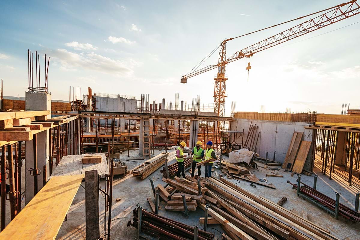 A construction site, with three men stood in the centre in discussion