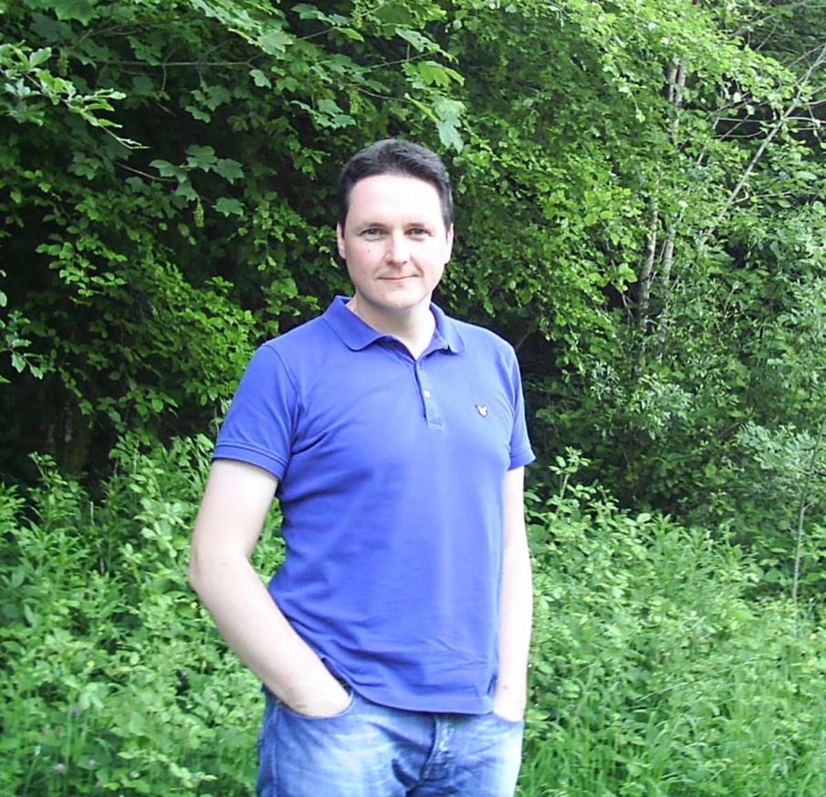 Jason Williams in a blue polo shirt stood by a tree