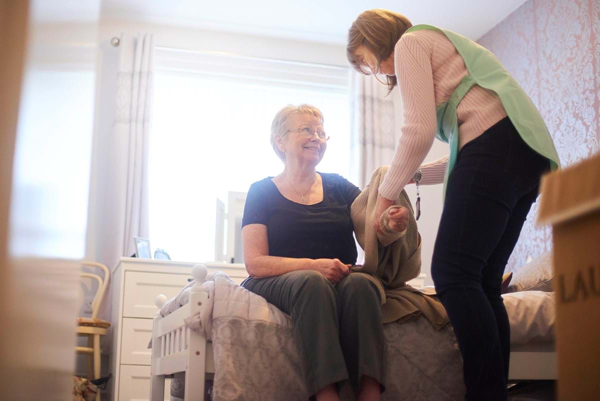 A female health worker helps dress and elderly woman